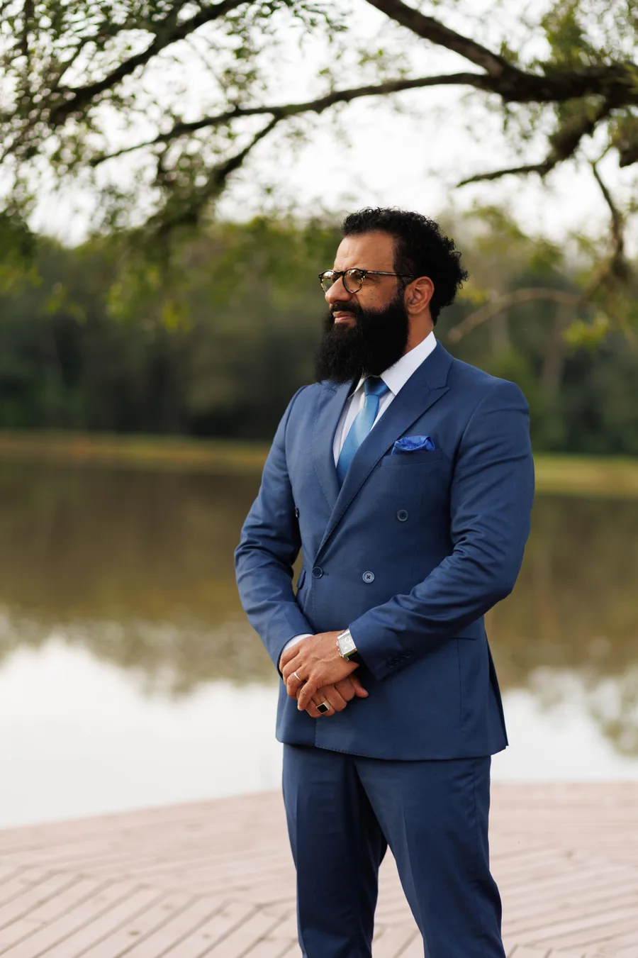 Douglas Proença, celebrante de casamentos, de terno azul à beira de um lago